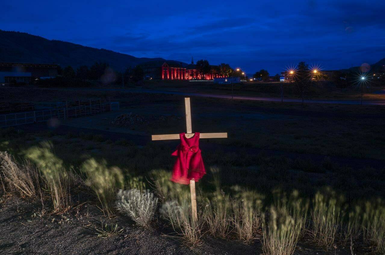 A child’s dress is seen on a cross outside the Residential School in Kamloops, B.C., Saturday, June, 13, 2021. The shishalh Nation on British Columbia’s Sunshine Coast says ground-penetrating radar has identified what are believed to be 40 unmarked graves of children on the site of the former St. Augustine’s Residential School. THE CANADIAN PRESS/Jonathan Hayward