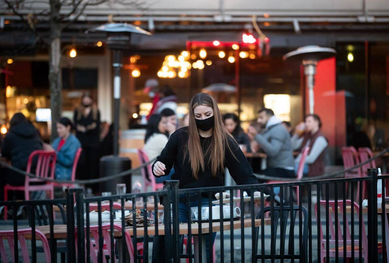 A server clears a table on a patio at a restaurant, in Vancouver, on Friday, April 2, 2021. A new study by the Canadian Federation of Independent Business found the average small business owner is working the equivalent of an eight-day workweek due to staffing challenges, with the issue especially prevalent in Western Canada. THE CANADIAN PRESS/Darryl Dyck