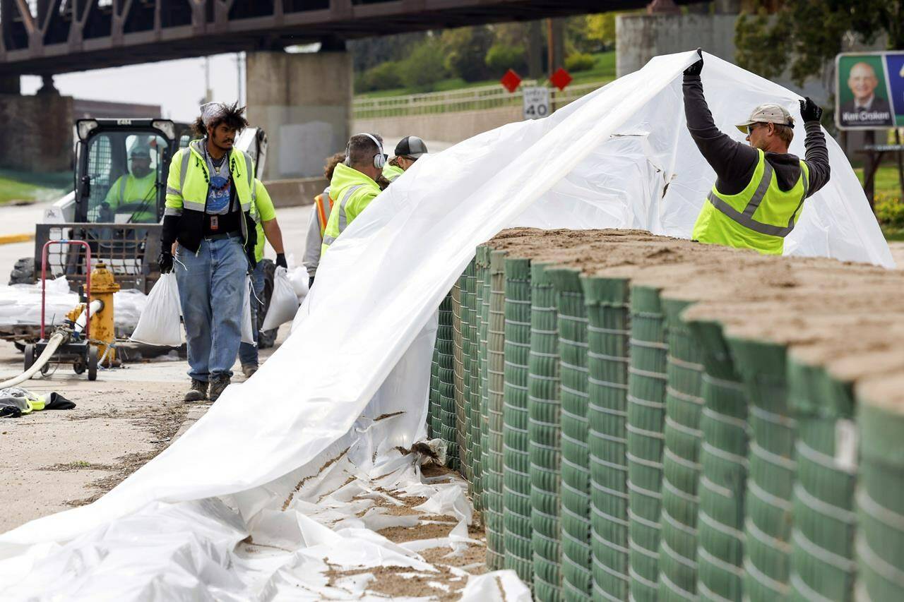 Workers lift a tarp over a HESCO sand barrier along River Drive in Davenport, Iowa, as the city prepares for flooding from the Mississippi River, Tuesday, April 25, 2023. (Nikos Frazier/Quad City Times via AP)