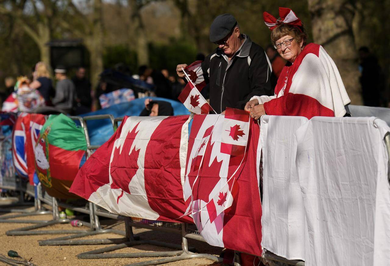 Bernadette Christie, right, and her husband Bruce Christie of Grand Prairie, Alta., hang their Canadian flags along the fence where she and her husband are camped out days before the official coronation of King Charles III near Buckingham Palace along the Mall in London on Wednesday, May 3, 2023. The Prime Minister’s Office still has yet to announce which eminent Canadians will be invited to join him for the coronation of King Charles in just three days. THE CANADIAN PRESS/Nathan Denette