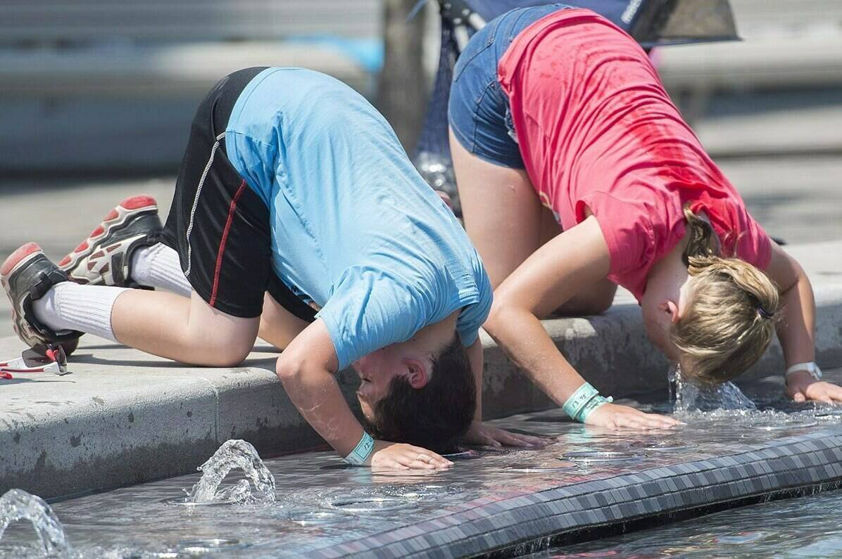 FILE - B.C. could be in for some “seasonally unusual” temperatures this weekend, but officials aren’t expecting a heat dome like what was experienced in 2021. A boy and girl dunk their heads in a water fountain during a heat wave in Montreal, Monday, July 2, 2018. THE CANADIAN PRESS/Graham Hughes