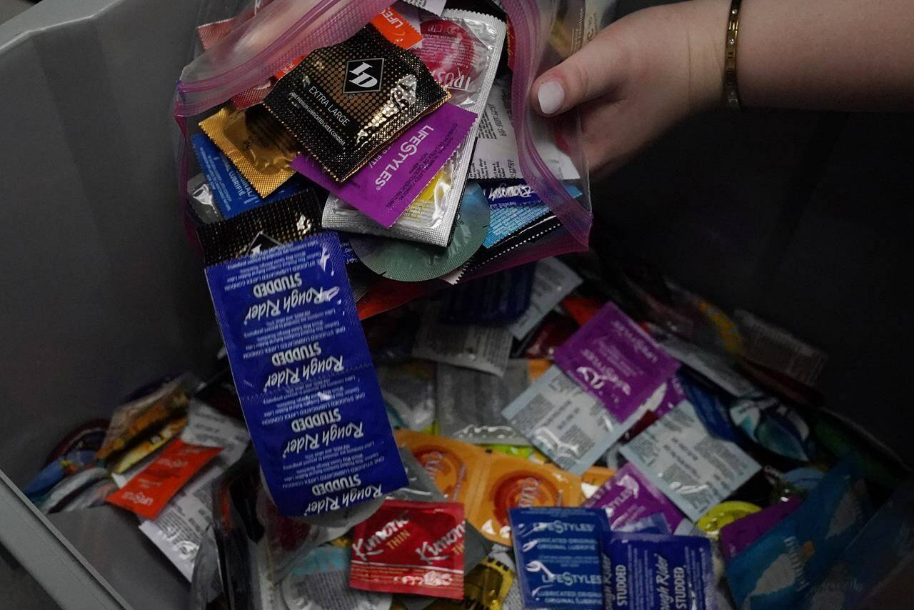 Abby Tow, a Sexual Health Peer Educator at the University of Oklahoma, dumps condoms into a container at the health center on campus, Wednesday, May 10, 2023, in Norman, Okla. Tow said she wonders if helicopter parenting has played a role in what she calls the “baby-fication of our generation”. (AP Photo/Sue Ogrocki)