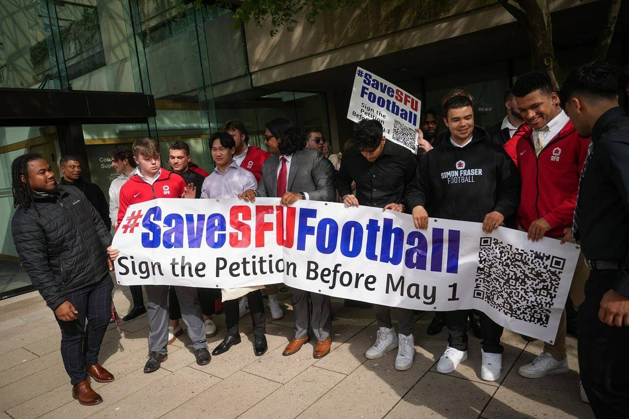 Simon Fraser University football team players hold a banner after attending a hearing at B.C. Supreme Court, in Vancouver, on Monday, May 1, 2023. Simon Fraser University says it has appointed a special adviser to help determine the future of its cancelled football program.THE CANADIAN PRESS/Darryl Dyck
