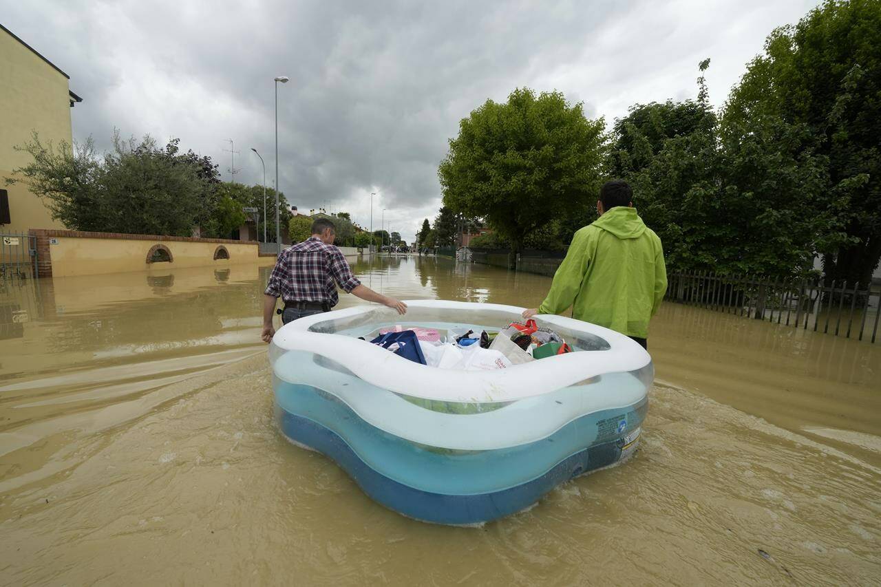 FILE - People use a plastic portable pool to carrie bags and personal effects in a flooded road of Lugo, Italy, May 18, 2023. The floods that sent rivers of mud tearing through towns in Italy’s northeast are another soggy dose of climate change’s all-or-nothing weather extremes, something that has been happening around the globe, scientists say. (AP Photo/Luca Bruno, File)
