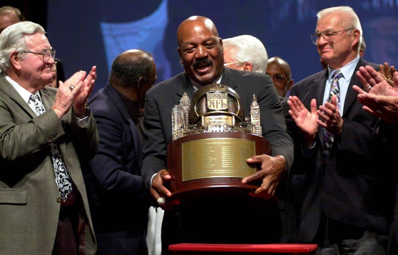 FILE - Jim Brown, center, picks up a trophy presented by NFL Commissioner Paul Tagliabue, to the members of Cleveland Browns 1964 Championship Team, at Severance Hall in Cleveland, Friday, Sept. 10, 2004. At left is Bernie Parish, and at right Paul Wiggin. The original trophy presented to the team after their 1964 victory over the Baltimore Colts is in the possession of the Green Bay Packers, who were the 1965 Championship Team. NFL legend, actor and social activist Jim Brown passed away peacefully in his Los Angeles home on Thursday night, May 18, 2023, with his wife, Monique, by his side, according to a spokeswoman for Brown’s family. He was 87. (AP Photo/Jamie-Andrea Yanak, File)