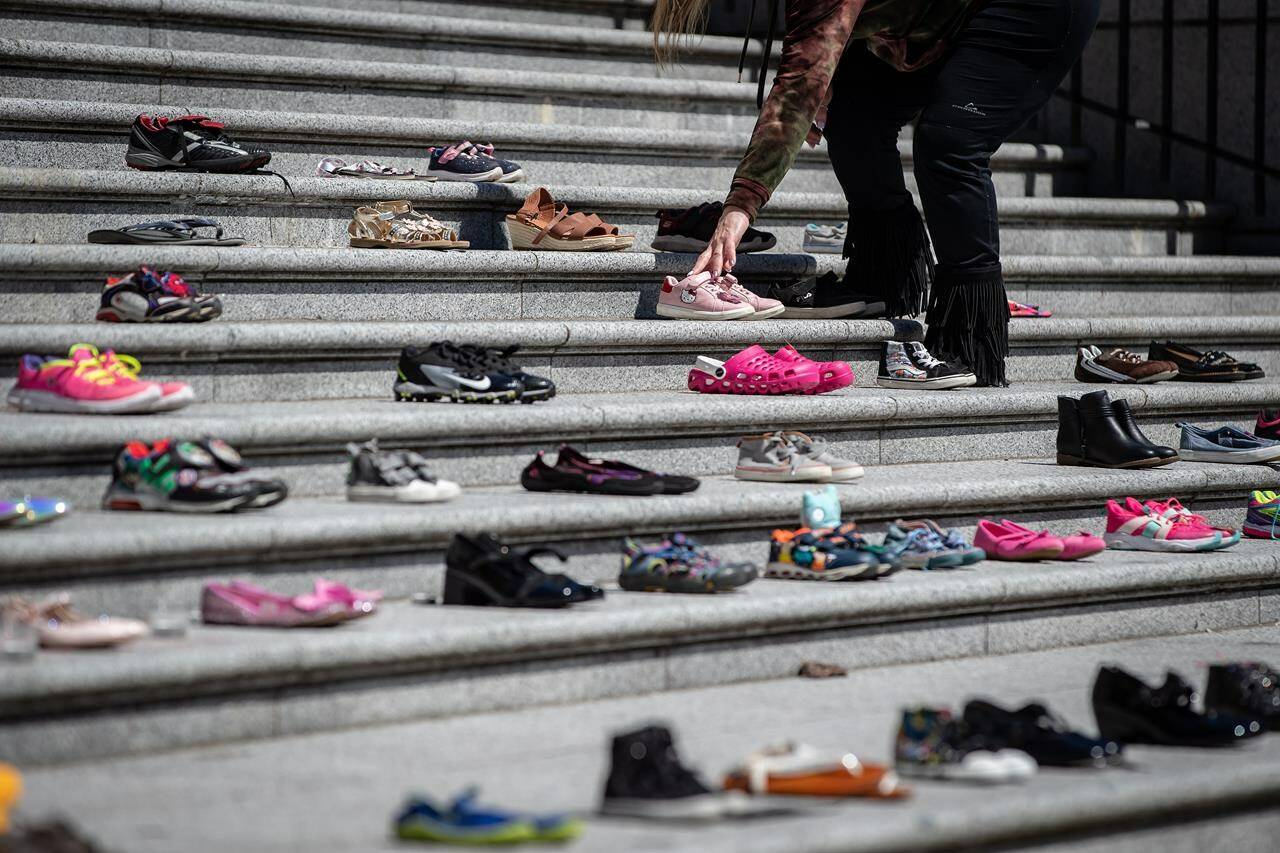 A woman places one of 215 pairs of children’s shoes on the steps of the Vancouver Art Gallery as a memorial to the 215 children whose remains have been found buried at the site of a former residential school in Kamloops, in Vancouver, B.C., Friday, May 28, 2021. THE CANADIAN PRESS/Darryl Dyck