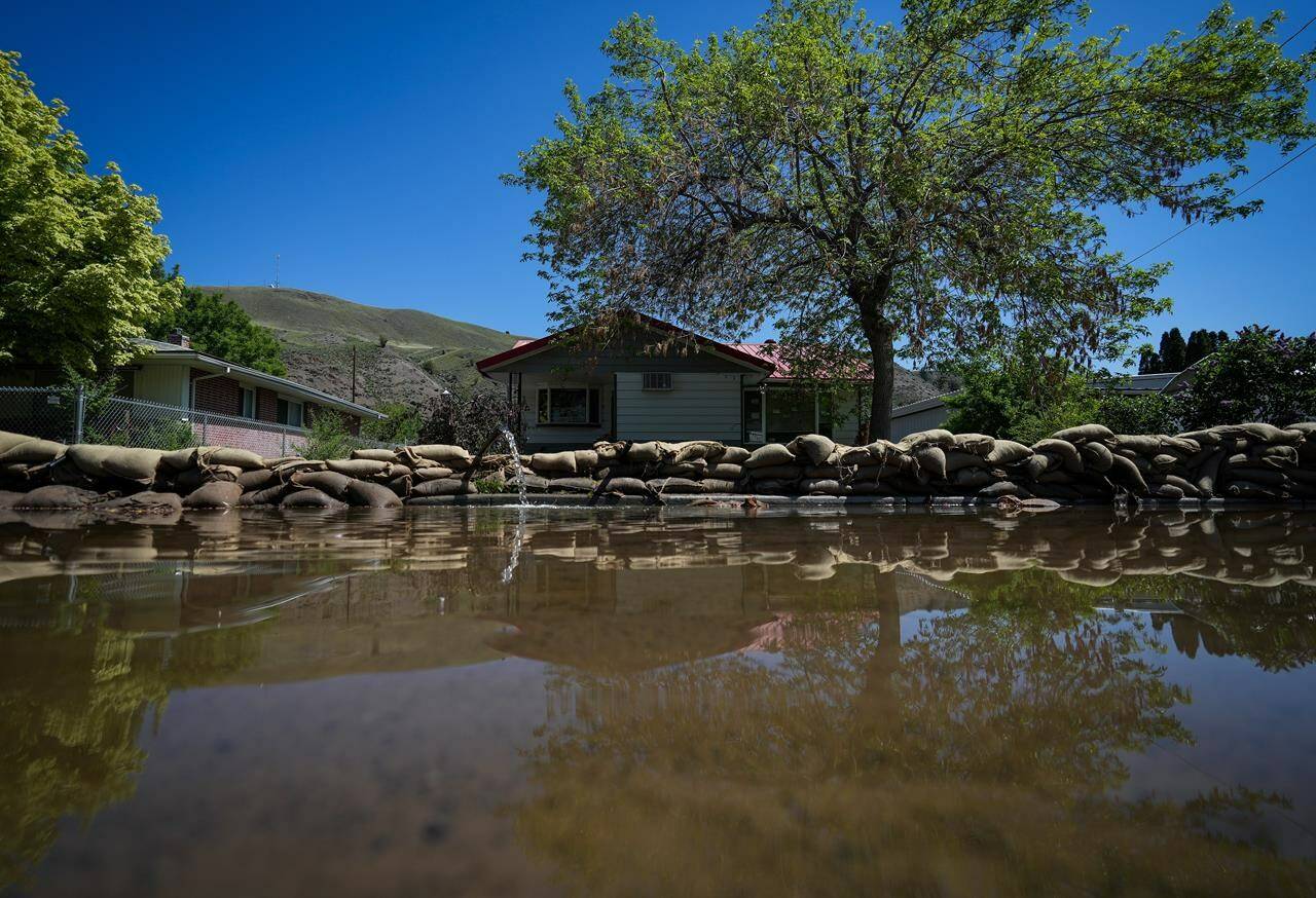 Water is pumped out from a flooded home near the Bonaparte River as sandbags line a sidewalk in Cache Creek, B.C., on May 14, 2023. THE CANADIAN PRESS/Darryl Dyck