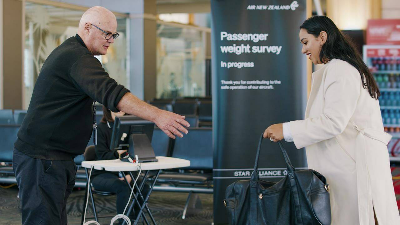 In this photo provided by Air New Zealand, a woman hands her bag to a staff member to be weighed ahead of a flight in Auckland, New Zealand, on May 29, 2023. New Zealand's national airline is asking people to step on the scales before they board international flights. Air New Zealand says it wants to weigh 10,000 passengers as part of a monthlong survey to better estimate the weight and balance of its planes. (Air New Zealand via AP)