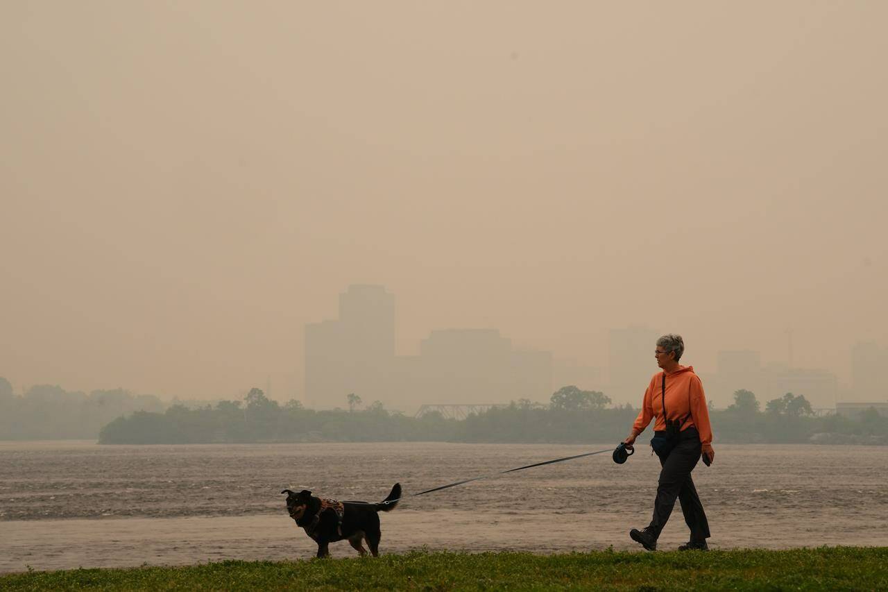 A woman walks her dog along the Ottawa River in Ottawa as smoke from wildfires obscures Gatineau, Que., in the distance on Tuesday, June 6, 2023. THE CANADIAN PRESS/Sean Kilpatrick
