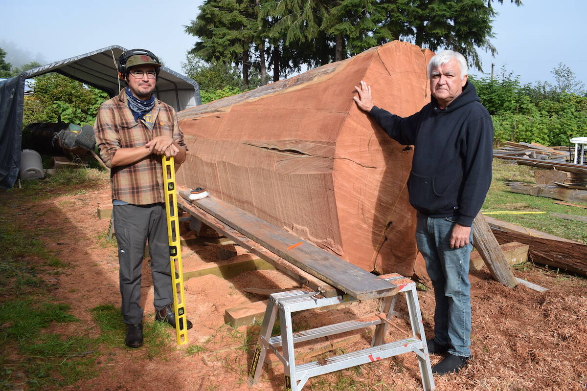 Apprentice carver Rey Dickie and master carver Stan Hunt stand next to the log that would be carved into a monument to remember Indigenous children who died at residential schools. (Tyson Whitney - North Island Gazette)