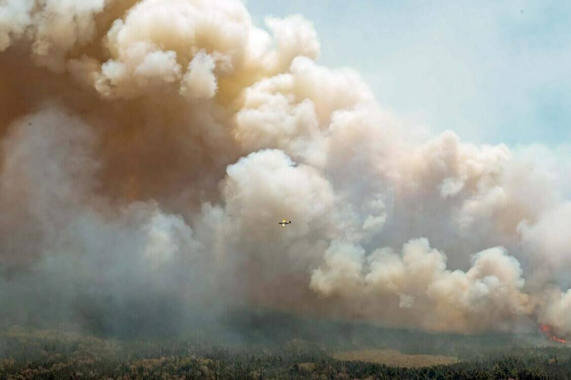 In this aerial image, an aircraft, centre, flies near a wildfire burning near Barrington Lake in Shelburne County, Nova Scotia, on Wednesday, May 31, 2023. THE CANADIAN PRESS/HO-Communications Nova Scotia **MANDATORY CREDIT**