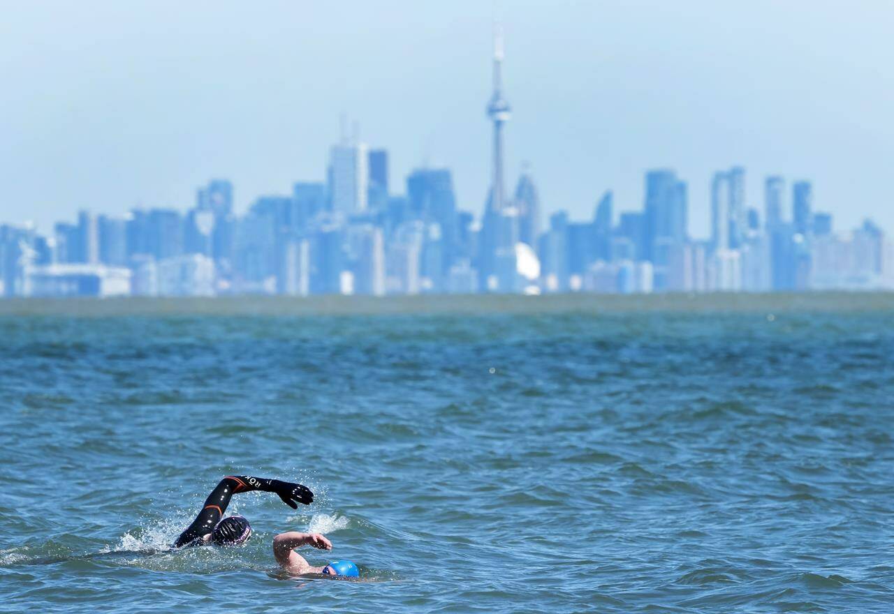 People swim in the frigid waters of Lake Ontario overlooking The City of Toronto’s skyline in Mississauga, Ont., Sunday, April 2, 2023. THE CANADIAN PRESS/Nathan Denette