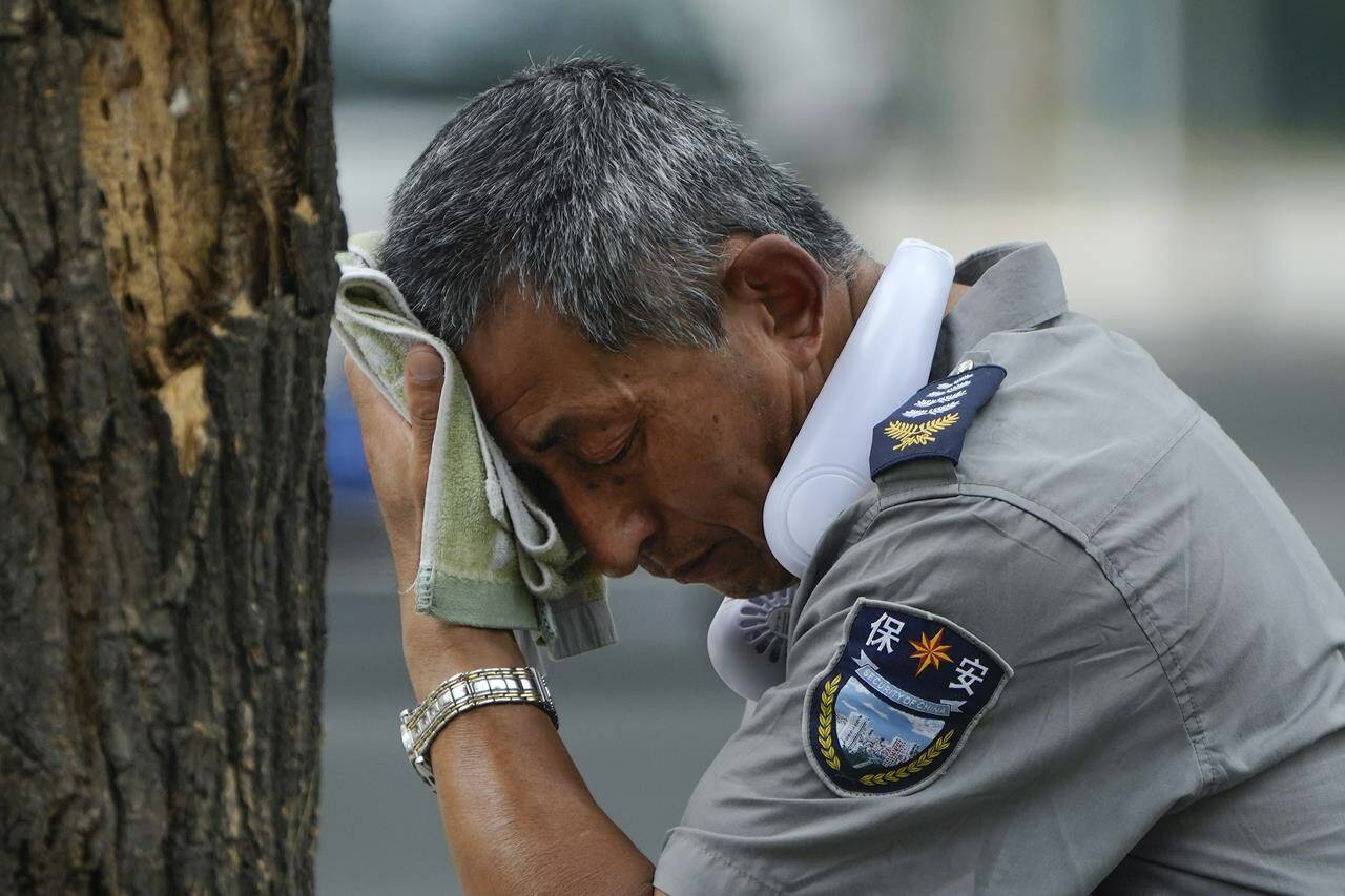 A security guard wearing an electric fan on his neck wipes his sweat on a hot day in Beijing, Monday, July 3, 2023. Heavy flooding has displaced thousands of people around China as the capital had a brief respite from sweltering heat. Beijing reported 9.8 straight days when the temperature exceeded 35 C (95 F), the National Climate Center said Monday. (AP Photo/Andy Wong)