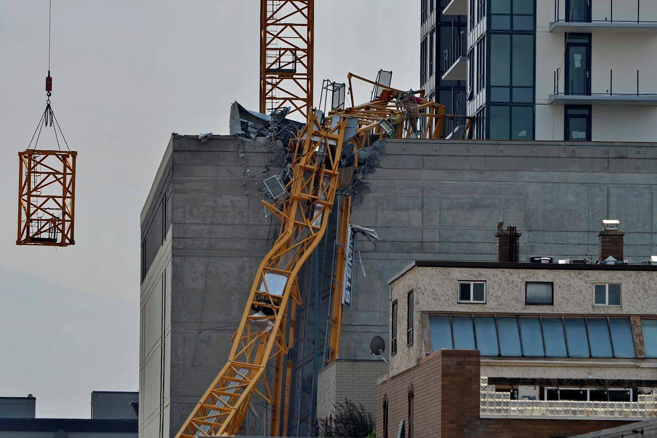 A section (left) of the vertical column of a construction crane is lowered past the mangled section of the fallen boom in Kelowna, B.C., Wednesday, July 14, 2021, following a fatal collapse of the crane on Monday. Evacuation orders have been lifted for all but one building in downtown Kelowna as crews have completed dismantling what remained of a crane that collapsed, killing five people.THE CANADIAN PRESS/Desmond Murray