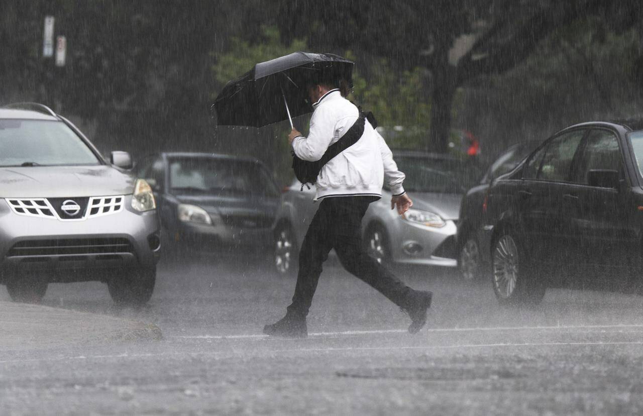 A pedestrians runs through a rainstorm Thursday, July 13, 2023 in Montreal. Power outages persist in the Montreal area after severe thunderstorms ripped through southern Quebec on Thursday, downing trees, snapping poles and breaking wires. THE CANADIAN PRESS/Ryan Remiorz