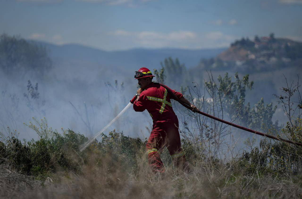 A firefighter directs water on a grass fire burning on an acreage behind a residential property in Kamloops, B.C., Monday, June 5, 2023. Firefighters battling British Columbia’s hundreds of wildfires have had more obstacles to deal with beyond the record-sized blazes. THE CANADIAN PRESS/Darryl Dyck