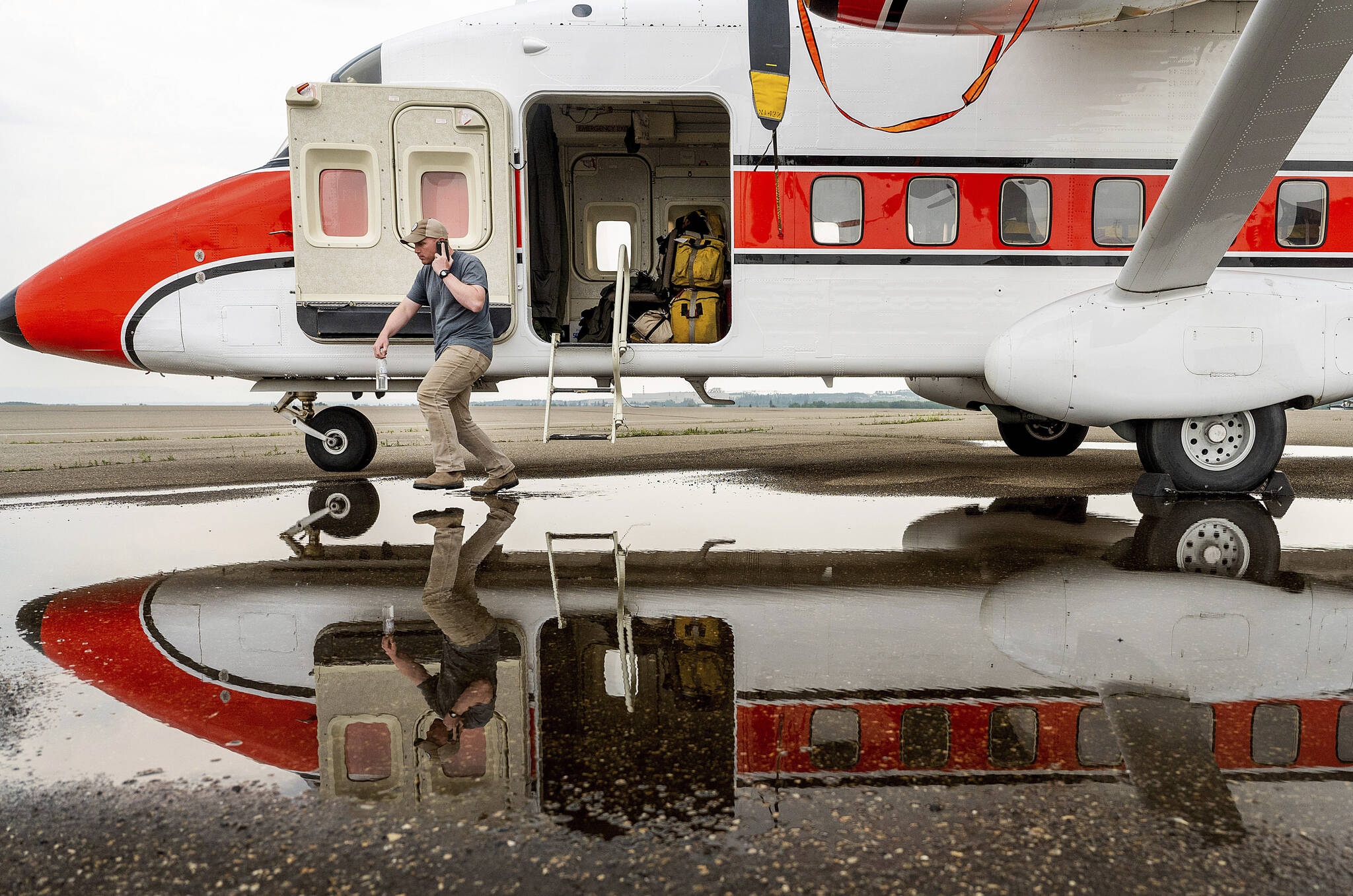 U.S. Forest Service co-pilot Matt Berggren steps through a puddle while exiting a plane in Fort St. John, British Columbia, Wednesday, July 5, 2023. U.S. smokejumpers are assisting Canadian firefighters battling blazes throughout the region. (AP Photo/Noah Berger)