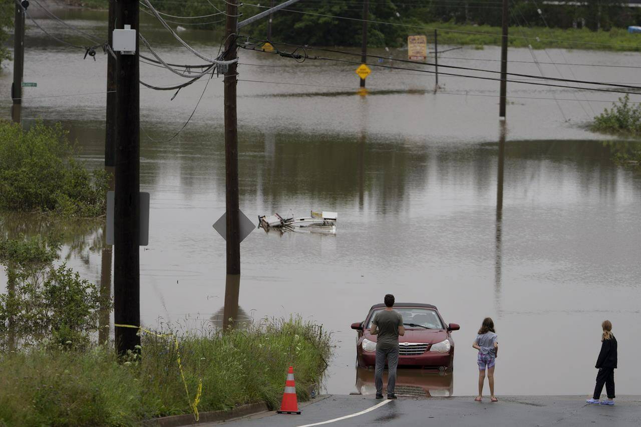 People stand at the edge of floodwater as vehicles are seen abandoned in water following a major rain event in Halifax on Saturday, July 22, 2023. A long procession of intense thunderstorms have dumped record amounts of rain across a wide swath of Nova Scotia, causing flash flooding, road washouts and power outages. THE CANADIAN PRESS/Darren Calabrese