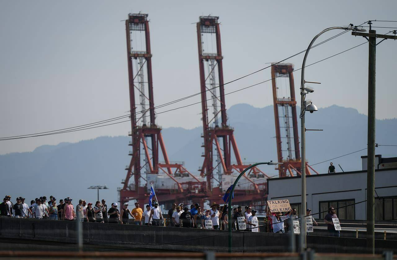Striking International Longshore and Warehouse Union Canada workers march to a rally as gantry cranes used to load and unload cargo containers from ships sit idle at port in Vancouver on Thursday, July 6, 2023. Thousands of workers at British Columbia’s ports will take off the day shift today to learn the details of an agreement struck between their union and employers. THE CANADIAN PRESS/Darryl Dyck