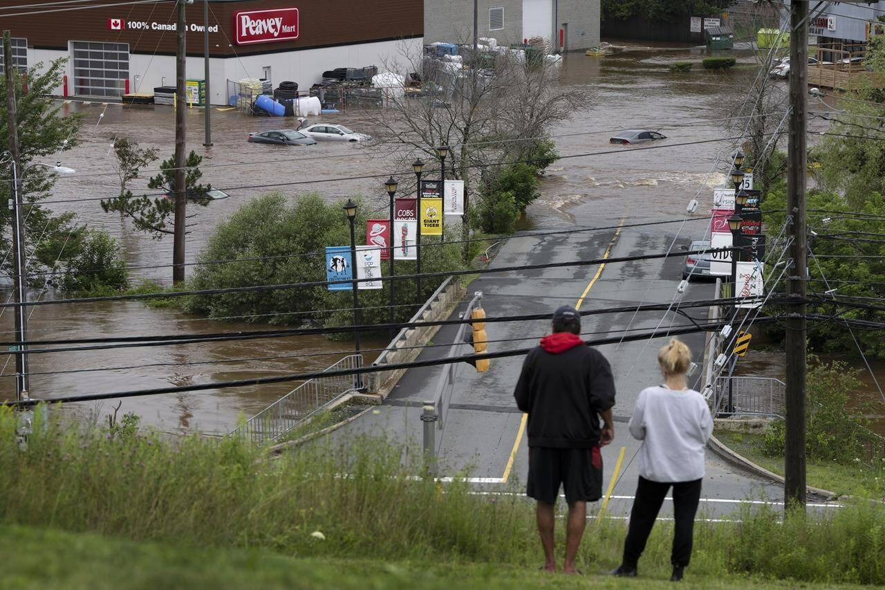 The cacophony caused by raging wildfires, searing heat and record-setting floods is caused by climate change, as world temperatures persistently increase, say experts. People stand on a hill surveying cars abandoned in floodwater in a mall parking lot following a major rain event in Halifax on Saturday, July 22, 2023. THE CANADIAN PRESS/Darren Calabrese