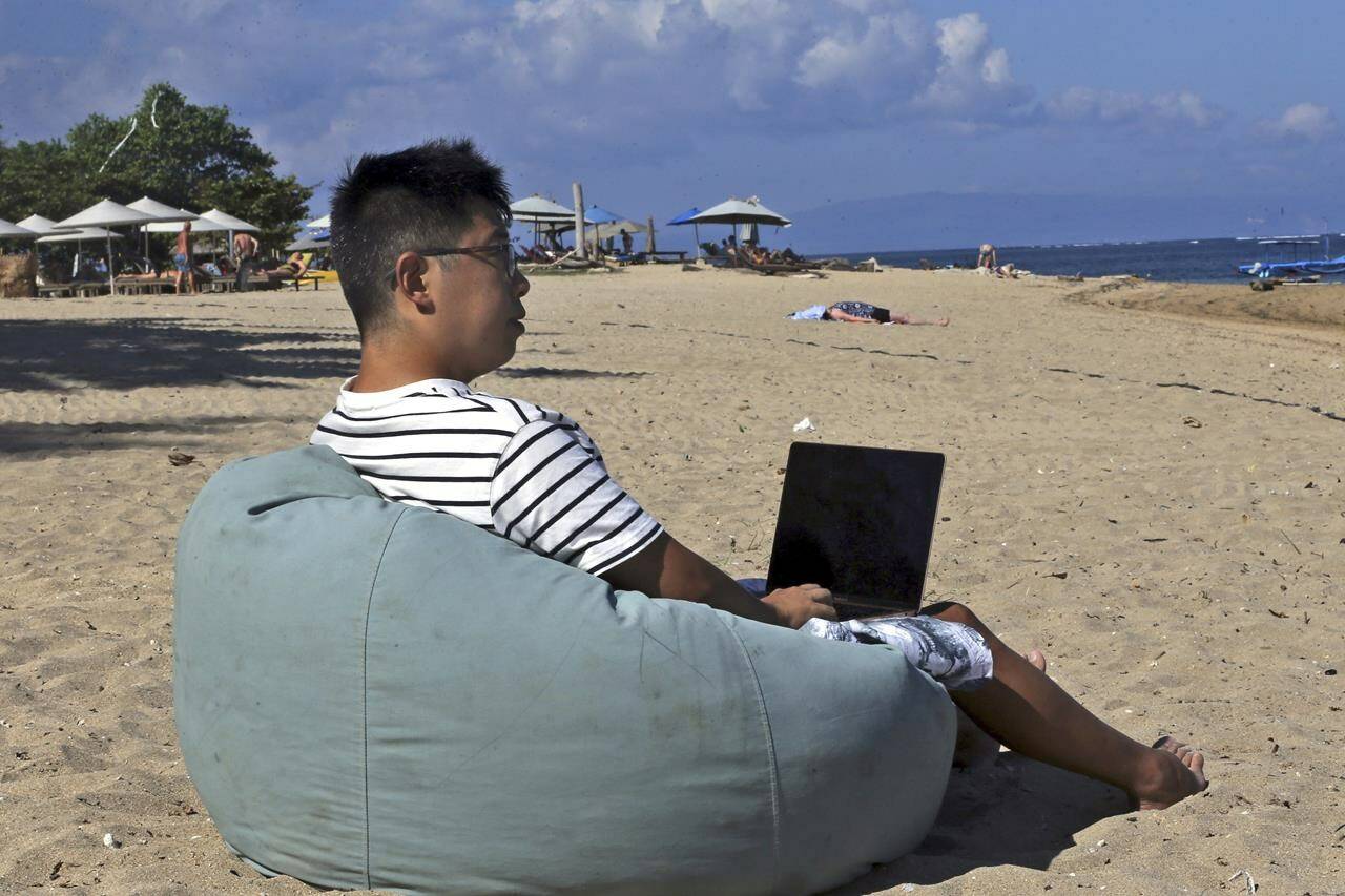 Chinese Armonio Liang sits on a beach as he works on his computer in Bali, Indonesia on Thursday, June 22, 2023. A growing number of young Chinese are moving overseas, frequently to Southeast Asia, to escape their homeland’s ultra-competitive work culture, limited opportunities and family pressures. There is no exact data on the number of the moves, the popular Chinese social media platform Xiaohongshu, hundreds of people have discussed relocating to Thailand. (AP Photo/Firdia Lisnawati)