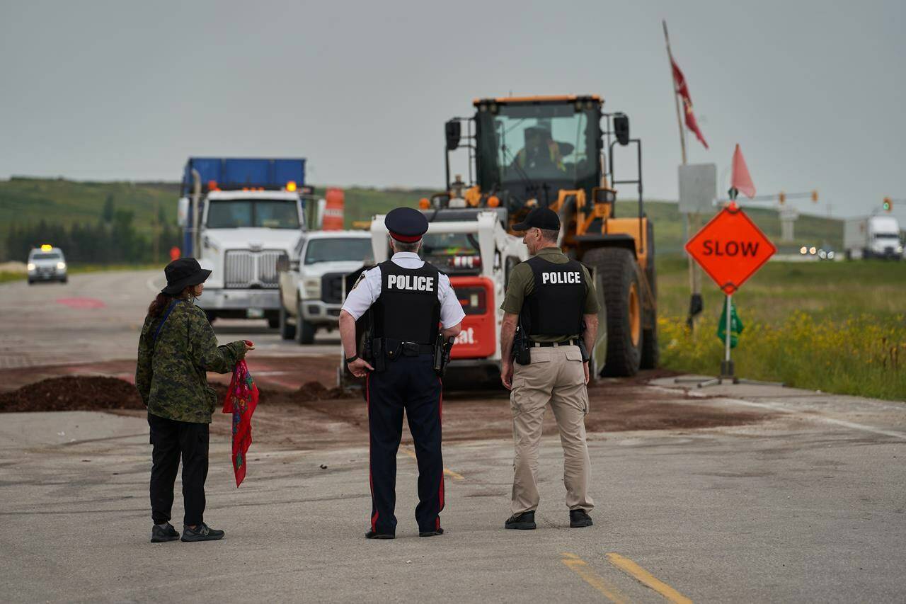 A protester speaks with Winnipeg police Insp. Gord Spado, centre, and Const. Brian Wurm, right, as City of Winnipeg workers remove a blockade on the main road into the Brady Road landfill just outside Winnipeg,Tuesday July 18, 2023. THE CANADIAN PRESS/David Lipnowski