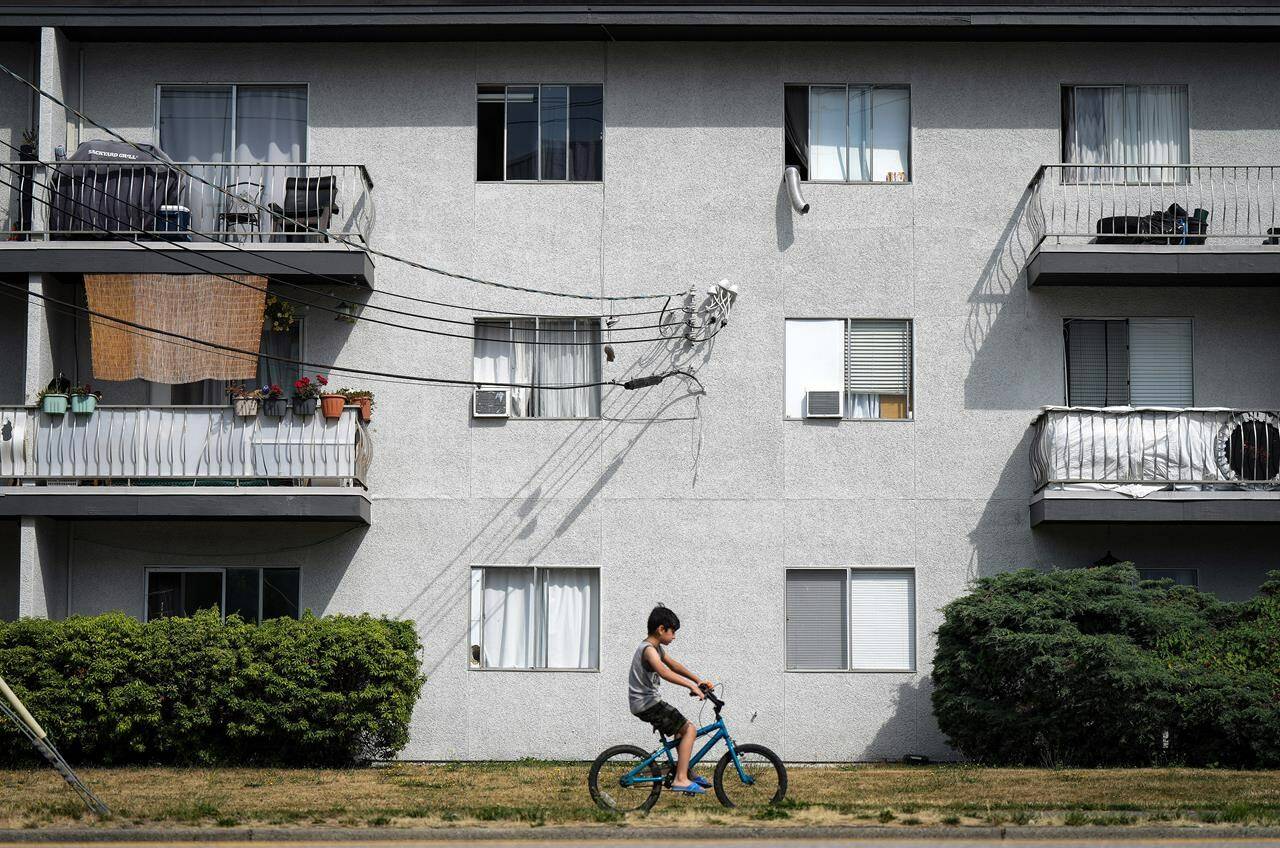 Window mounted air conditioners and exhaust hoses from portable units are seen in apartment windows, in Burnaby, B.C., on Saturday, August 5, 2023. THE CANADIAN PRESS/Darryl Dyck