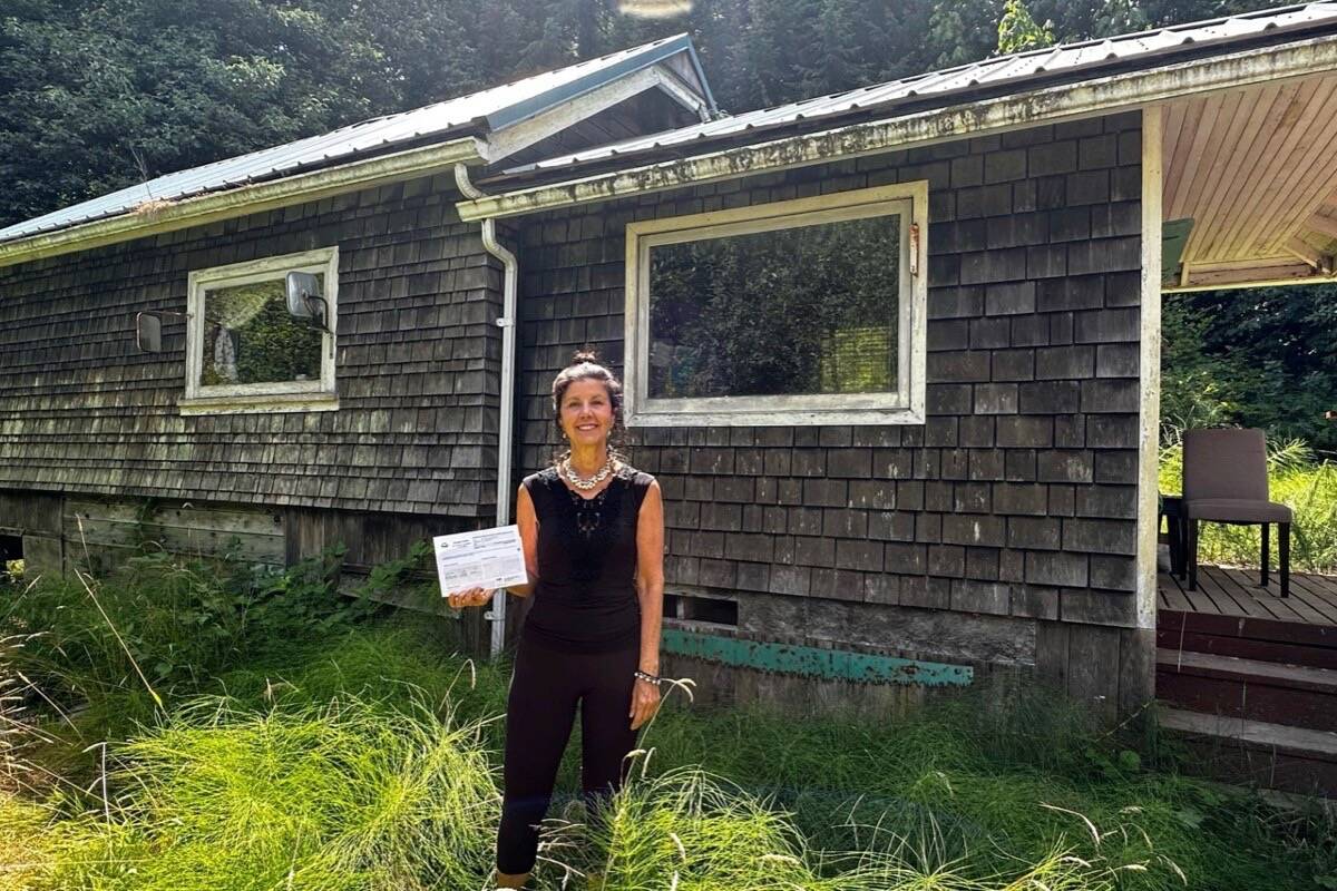 Shelley Robinson, a homeowner of waterfront property in Honeymoon Bay, holds a notice from the property assessment review panel upholding BC Assessment's valuation of the property at $2.3 million, despite the fact that the home and property are in a dilapidated state. (Jason Anson photo)