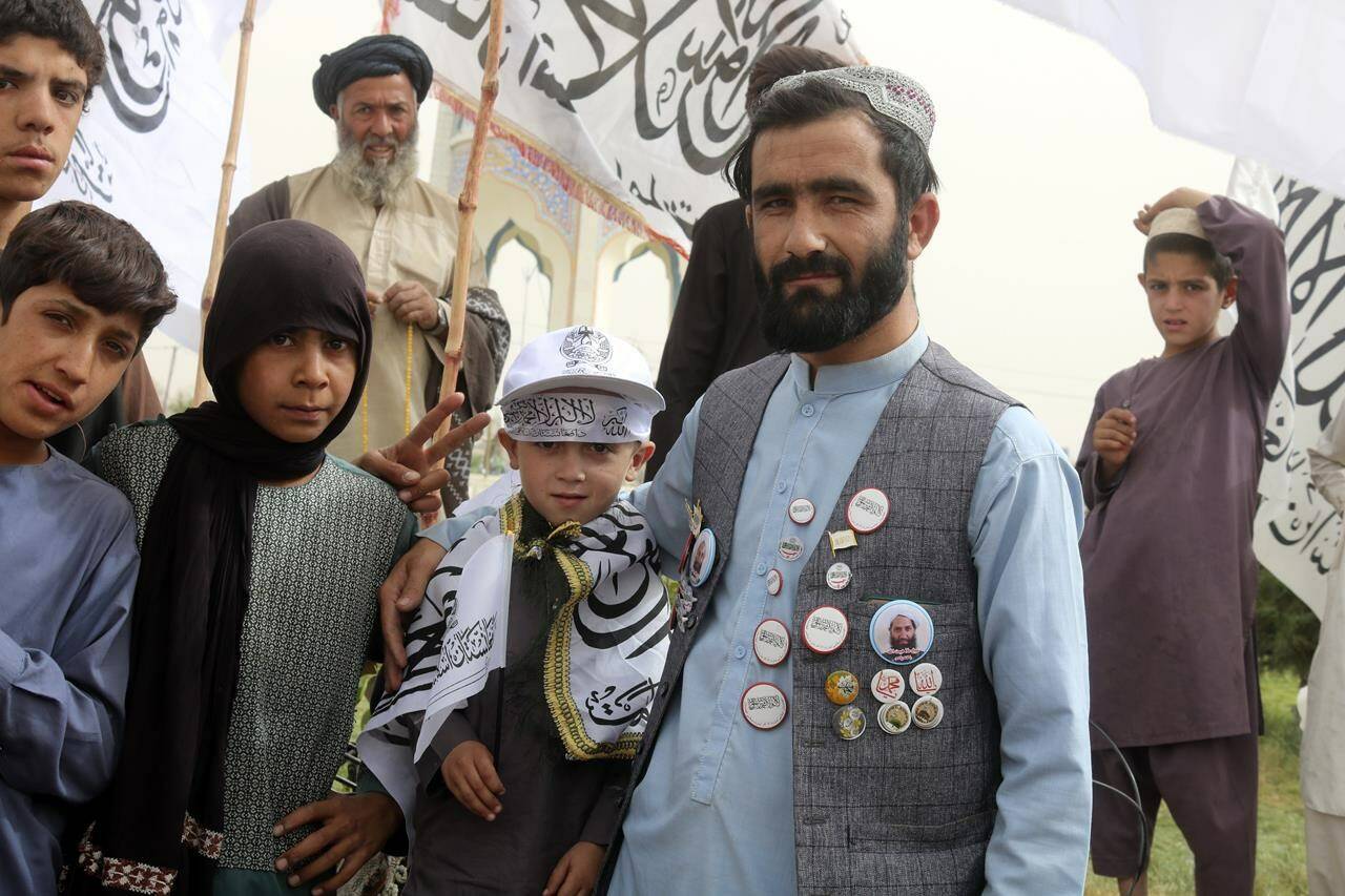 A supporter of Taliban shows off portraits of Taliban leader and flags he placed on his clothing during a celebration marking the second anniversary of the withdrawal of U.S.-led troops from Afghanistan, in Kandahar, south of Kabul, Afghanistan, Tuesday, Aug. 15, 2023. (AP Photo/Abdul Khaliq)