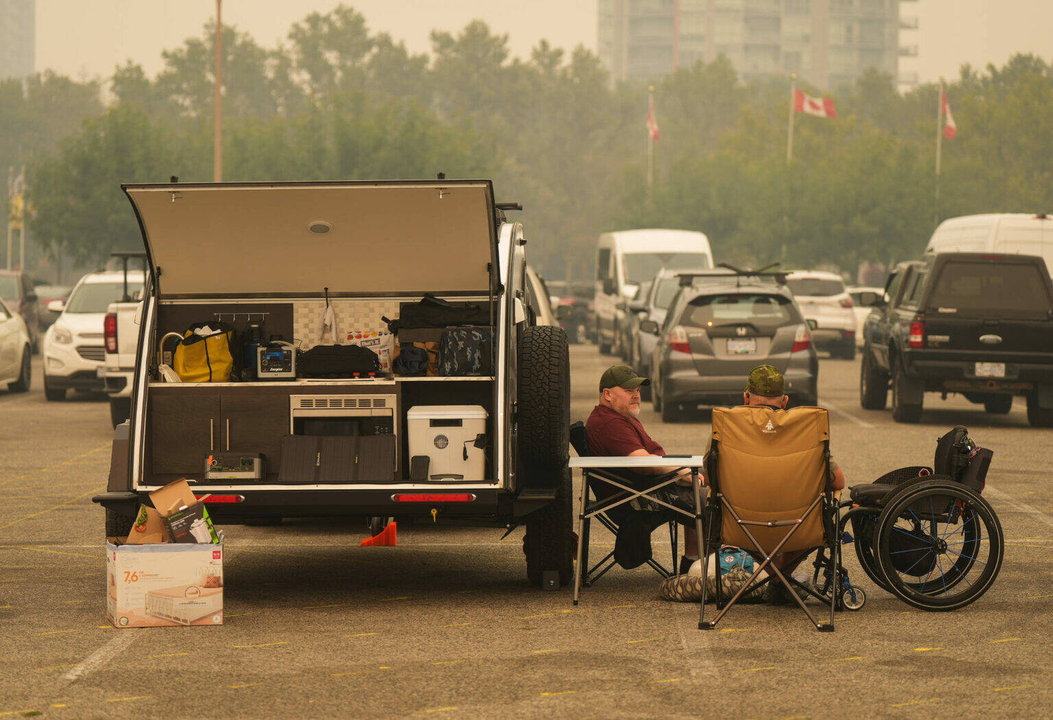 Wildfire evacuees Warren Pullen, left, and veteran Rob Pullen sit outside their trailer in the parking lot at an evacuation centre, in Kelowna, B.C., Saturday, Aug. 19, 2023. (THE CANADIAN PRESS/Darryl Dyck)