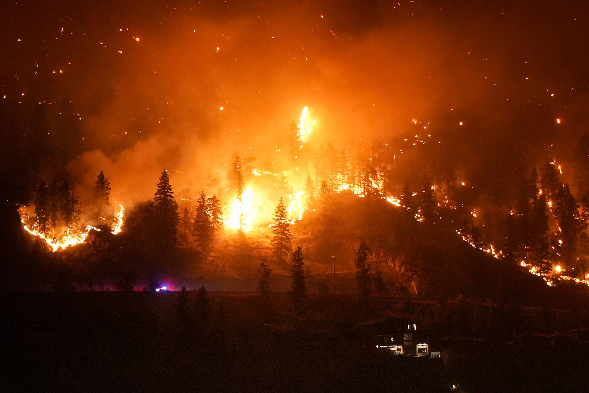 The McDougall Creek wildfire burns on the mountainside above a lakefront home, in West Kelowna, B.C., on Friday, August 18, 2023. THE CANADIAN PRESS/Darryl Dyck