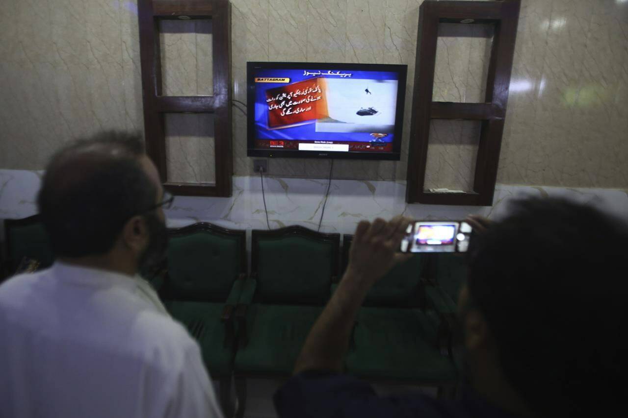 Members of media watch a news channel airing news regarding people trapped in a cable car, Tuesday, Aug. 22, 2023, at an office in Peshawar, Pakistan. A cable car carrying six children and two adults dangled hundreds of meters (feet) above the ground in a remote part of Pakistan after it broke on Tuesday, trapping the occupants for hours before rescuers arrived in helicopters to try to free them. (AP Photo/Muhammad Sajjad)