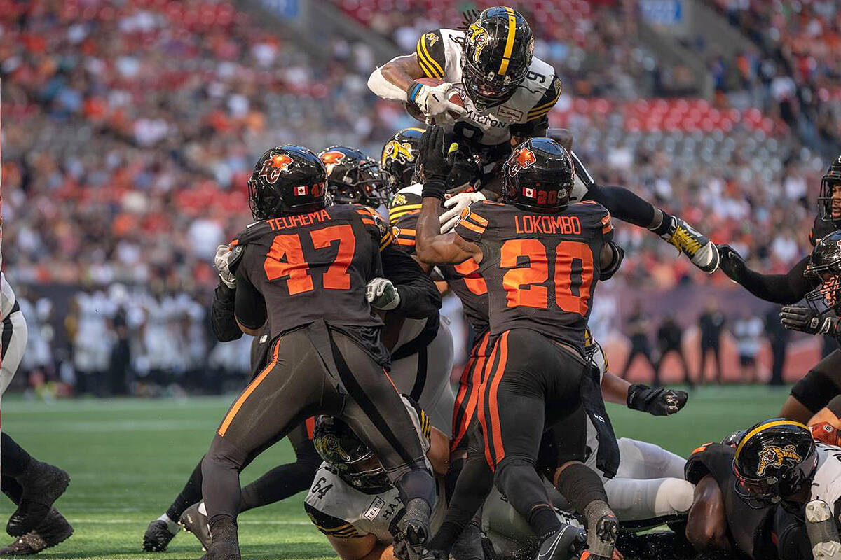 Hamilton Tiger-Cats quarterback Dane Evans (9) jumps over B.C. Lions’ Sione Teuhema (47) and Boseko Lokombo (20) to score a touchdown during first half CFL football action in Vancouver on Saturday, August 26, 2023. THE CANADIAN PRESS/Ethan Cairns