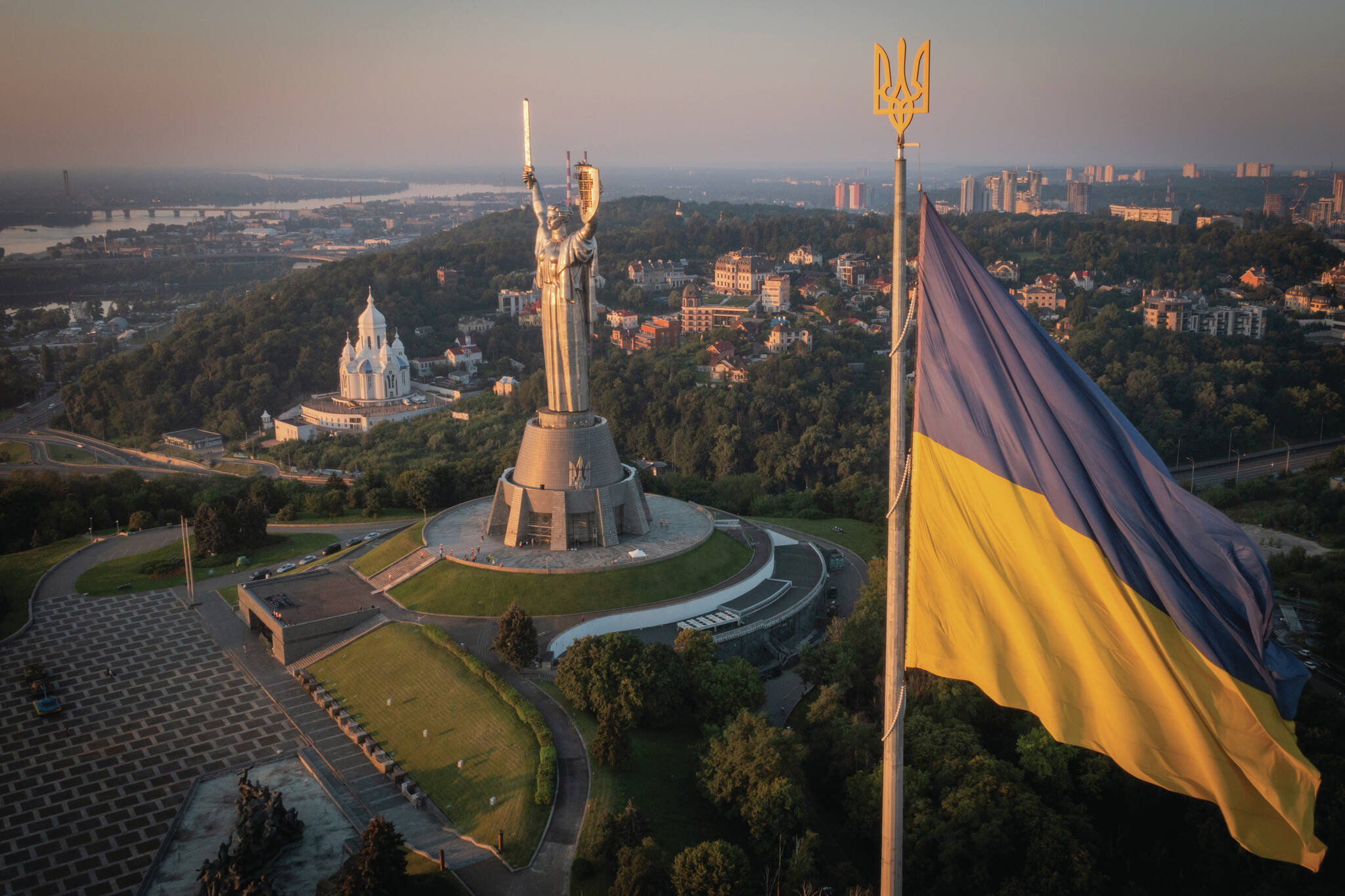 The national flag waves as workers install the Ukrainian coat of arms on the shield in the hand of the country’s tallest stature, the Motherland Monument, after the Soviet coat of arms was removed, in Kyiv, Ukraine, Sunday, Aug. 6, 2023. Ukraine is accelerating efforts to erase the vestiges of centuries of Soviet and Russian influence from the public space amid the Russian invasion of Ukraine by pulling down monuments and renaming hundreds of streets to honor home-grown artists, poets, military chiefs, and independence leaders. (AP Photo/Efrem Lukatsky)