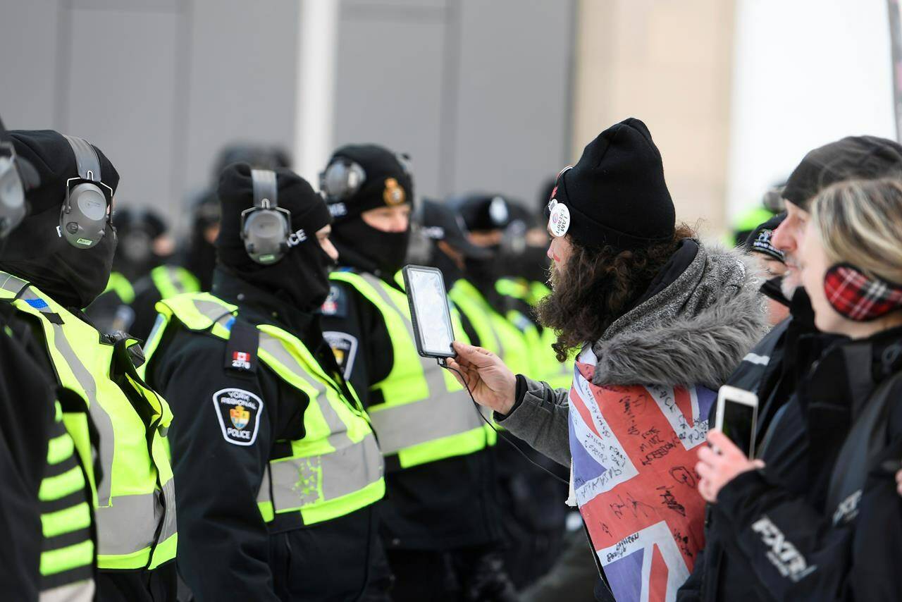 A protester films a line of police officers as they assemble by the Rideau Centre near the truck blockade in Ottawa, on Friday, Feb. 18, 2022. THE CANADIAN PRESS/Justin Tang