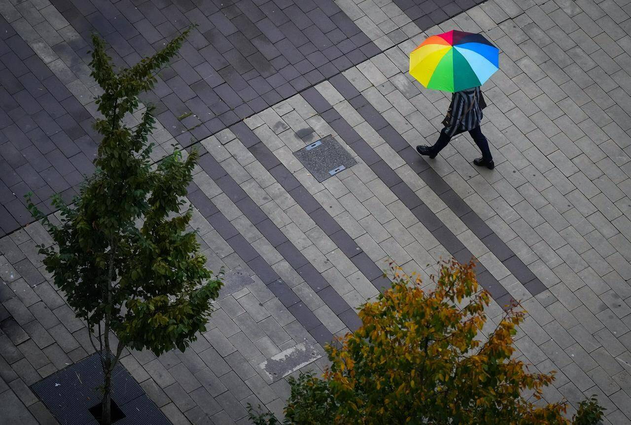 A pedestrian carries an umbrella as light rain falls in Surrey, B.C., on Friday, Oct. 21, 2022. Environment Canada has issued wind warnings for much of British Columbia’s coast ahead of a storm expected Monday. THE CANADIAN PRESS/Darryl Dyck