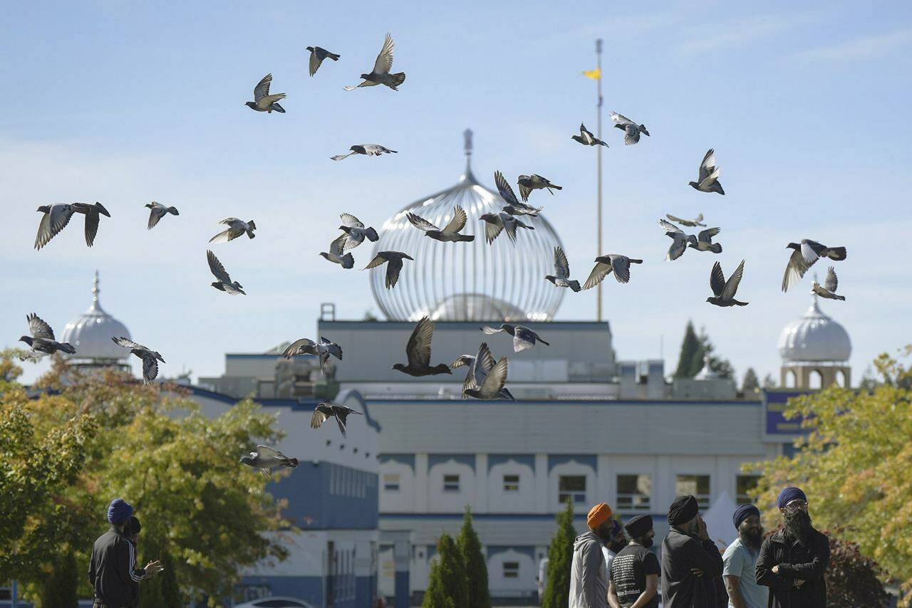 FILE - A flock of birds flies past as Moninder Singh, foreground right, a spokesperson for the British Columbia Gurdwaras Council (BCGC), waits to speak to reporters outside the Guru Nanak Sikh Gurdwara Sahib in Surrey, British Columbia, Canada, on Monday, Sept. 18, 2023, where temple president Hardeep Singh Nijjar was gunned down in his vehicle while leaving the temple parking lot in June. Canada expelled a top Indian diplomat Monday as it investigates what Prime Minister Justin Trudeau called credible allegations that India’s government may have had links to the assassination in Canada of a Sikh activist. (Darryl Dyck/The Canadian Press via AP, File)