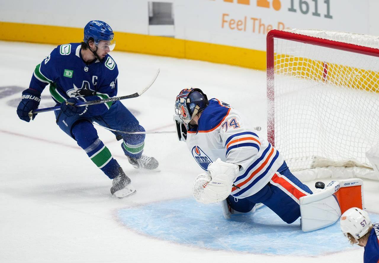 Vancouver Canucks’ Quinn Hughes, back left, scores his first goal against Edmonton Oilers goalie Stuart Skinner during the second period of a pre-season NHL hockey game in Vancouver, B.C., Saturday, Sept. 30, 2023. THE CANADIAN PRESS/Darryl Dyck