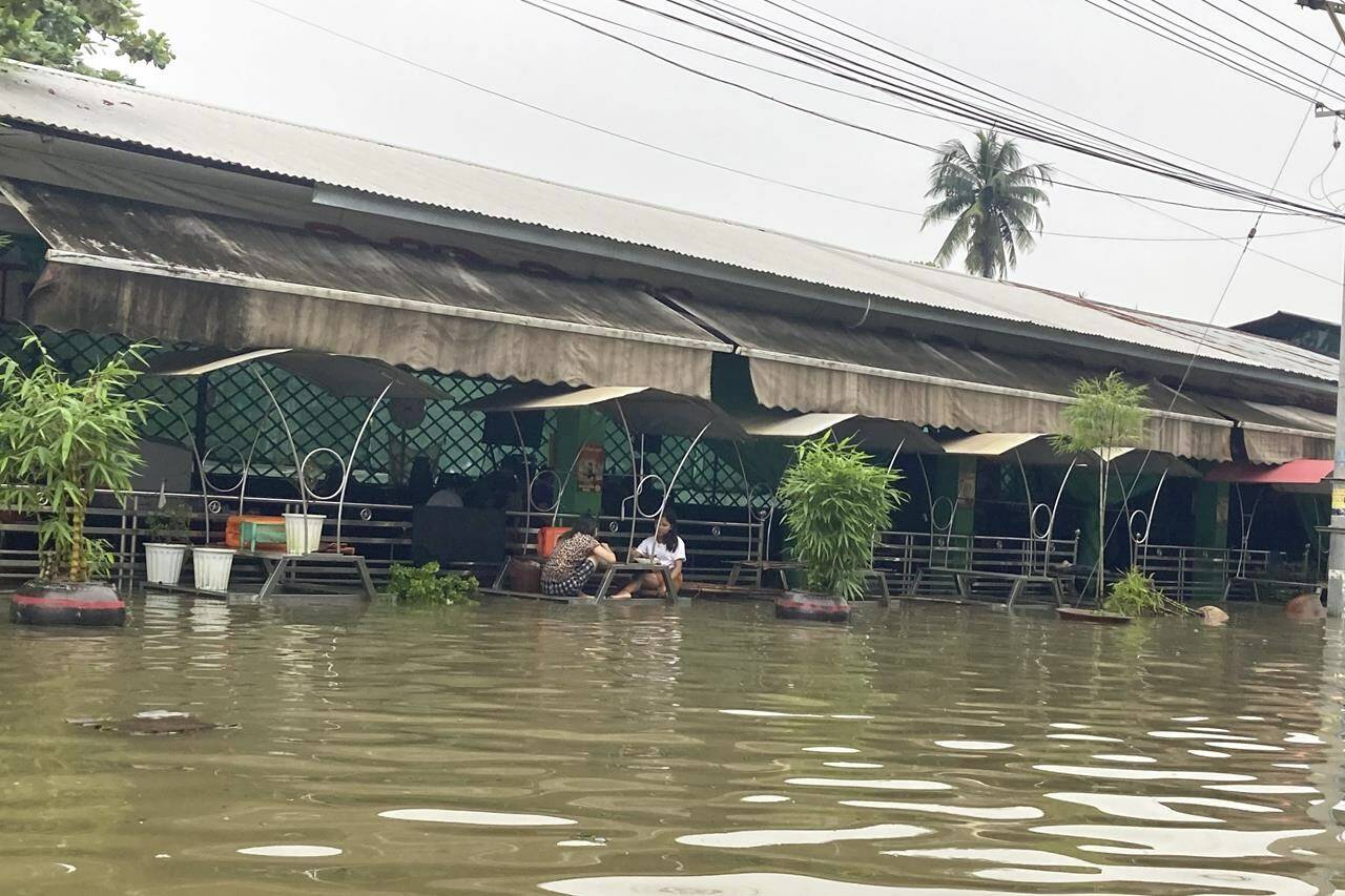 Two girls have foods at a restaurant on a flooded road in Bago, about 80 kilometers (50 miles) northeast of Yangon, Myanmar, Monday, Oct.9, 2023. Flooding triggered by heavy monsoon rains in Myanmar’s southern areas has displaced more than 10,000 people and disrupted traffic on the rail lines that connect the country’s biggest cities, officials and state-run media said Monday. (AP Photo/Thein Zaw)