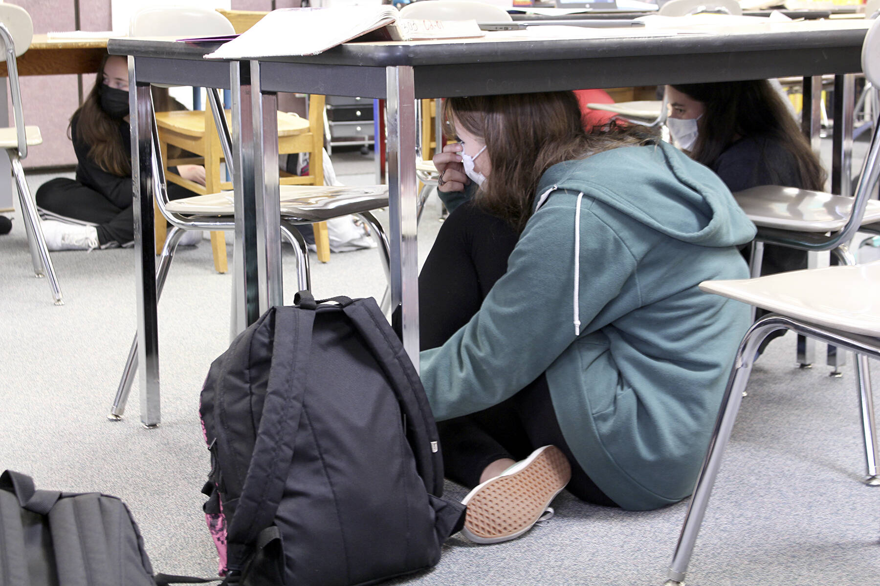 A student takes shelter under her table at school as part of the annual ShakeOut earthquake drill. The 2023 drill is Thursday, Oct. 19 at 10:19 a.m. (Black Press file photo)