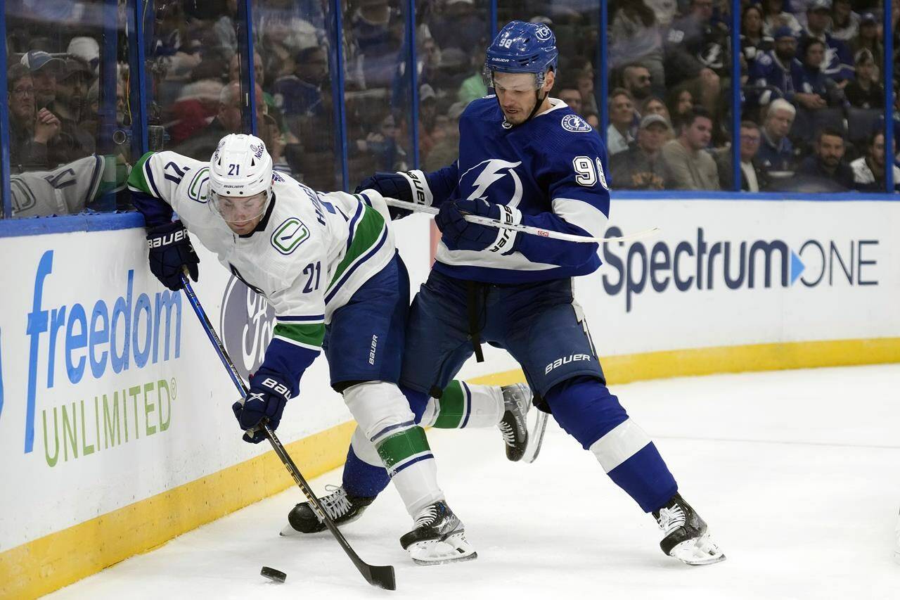Tampa Bay Lightning defenseman Mikhail Sergachev (98) knocks Vancouver Canucks left wing Nils Hoglander (21) off the puck during the first period of an NHL hockey game Thursday, Oct. 19, 2023, in Tampa, Fla. (AP Photo/Chris O’Meara)