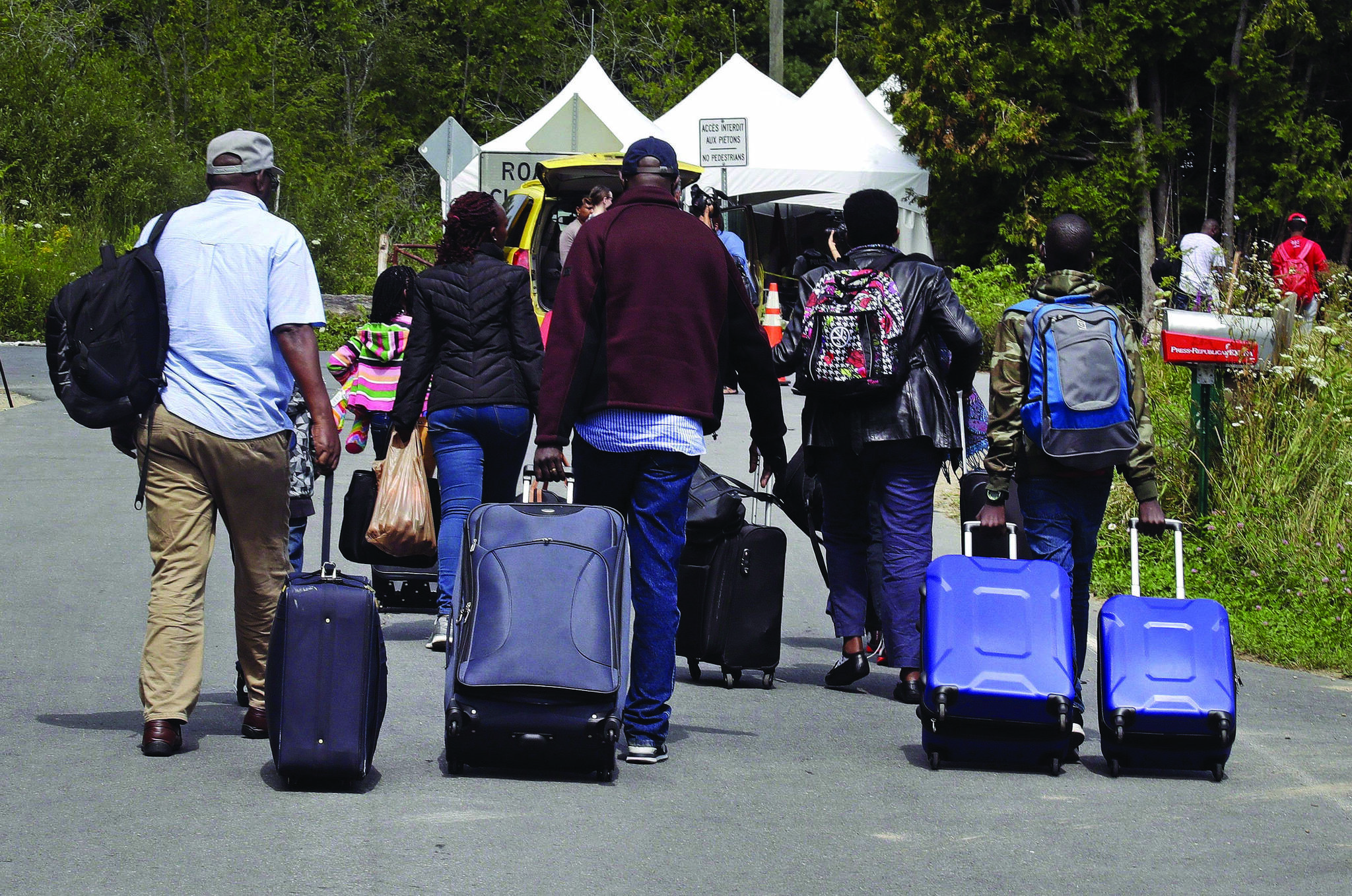 A newly released memo shows federal officials warned last spring that expanding a bilateral refugee pact to the entire Canada-U.S. border would likely fuel smuggling networks and encourage people to seek more dangerous, remote crossing routes. A family from Haiti approach a tent in Saint-Bernard-de-Lacolle, Quebec, stationed by Royal Canadian Mounted Police, as they haul their luggage down Roxham Road in Champlain, N.Y., on August 7, 2017. THE CANADIAN PRESS/AP, Charles Krupa