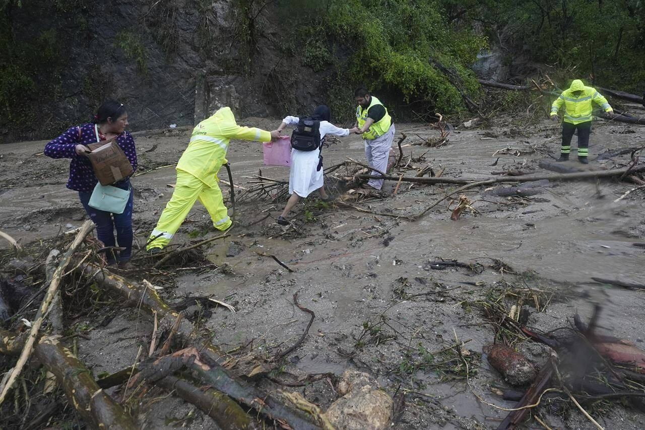 People get help crossing a highway blocked by a landslide triggered by Hurricane Otis near Acapulco, Mexico, Wednesday, Oct. 25, 2023. The hurricane turned from mild to monster in record time, and scientists are struggling to figure out how — and why they didn’t see it coming. (AP Photo/Marco Ugarte)