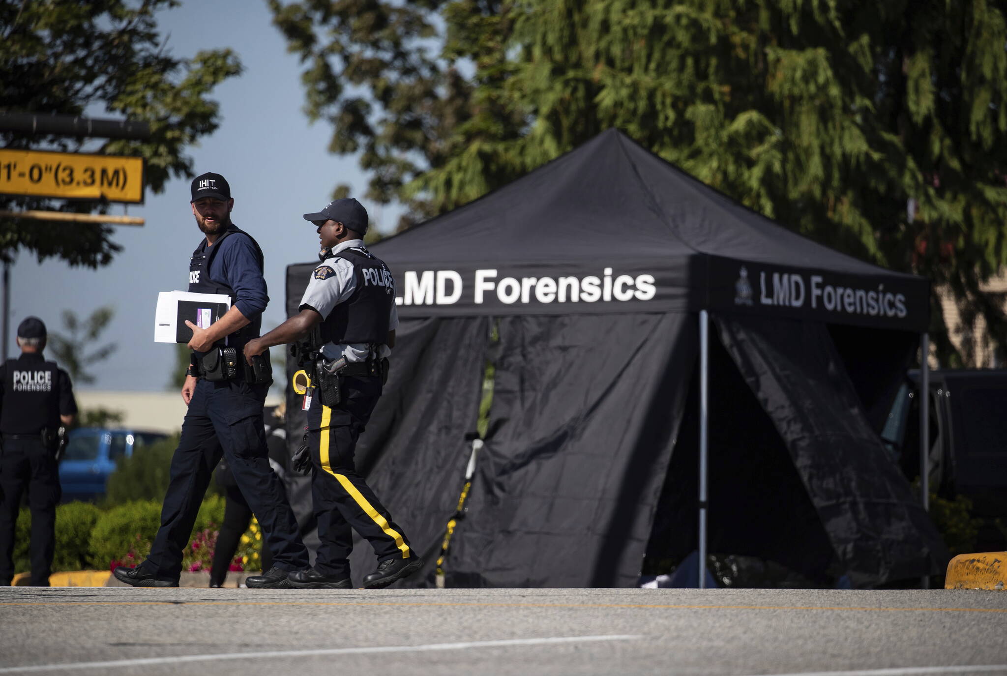 RCMP officers talk as a tent covers a body at the scene of a shooting in Langley, British Columbia, Monday, July 25, 2022. (Darryl Dyck/The Canadian Press via AP)