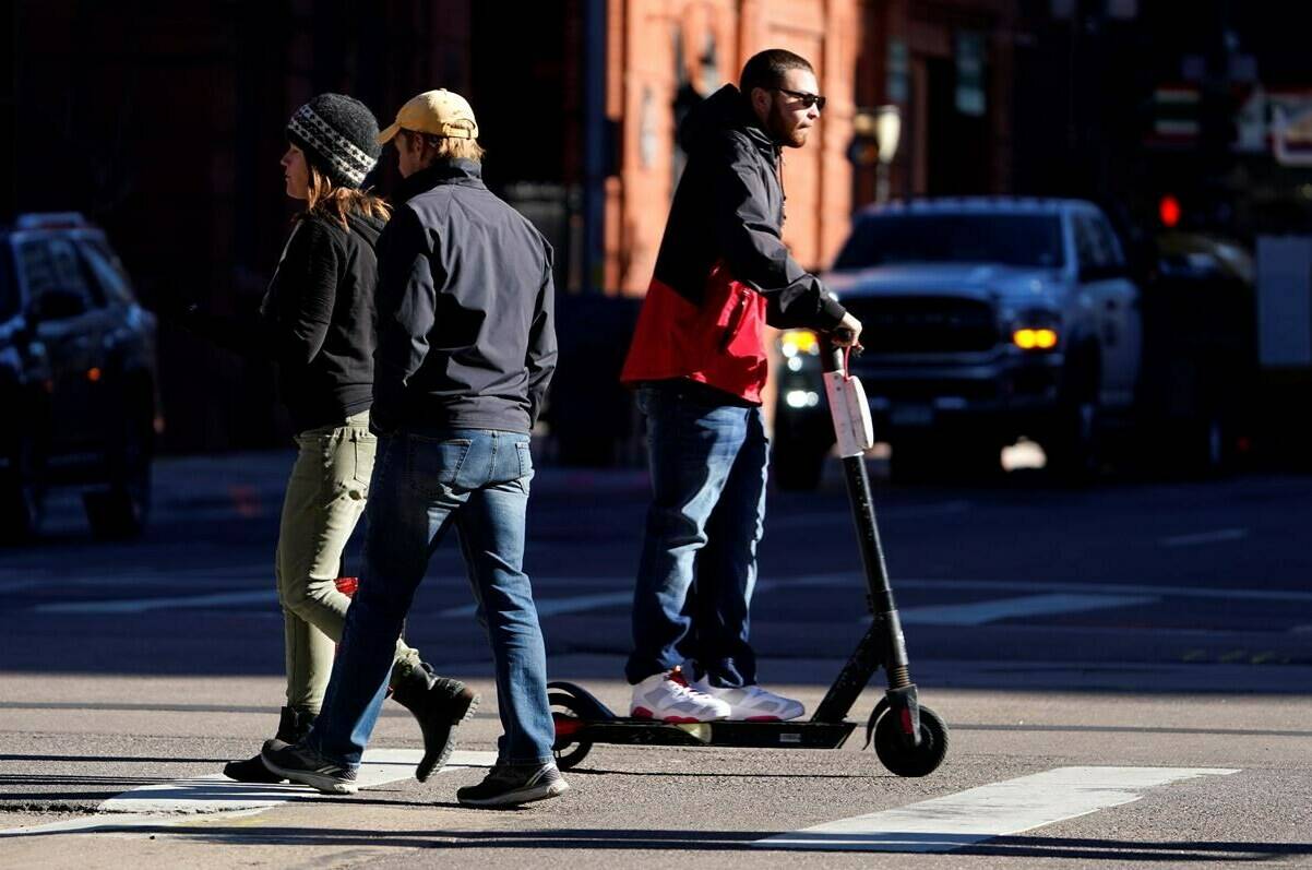 An electric scooter driver dodges pedestrians as they cross an intersection in downtown Denver. British Columbia will be kicking off a four-year review in April on the emerging mode of transportation. THE CANADIAN PRESS/AP-David Zalubowski