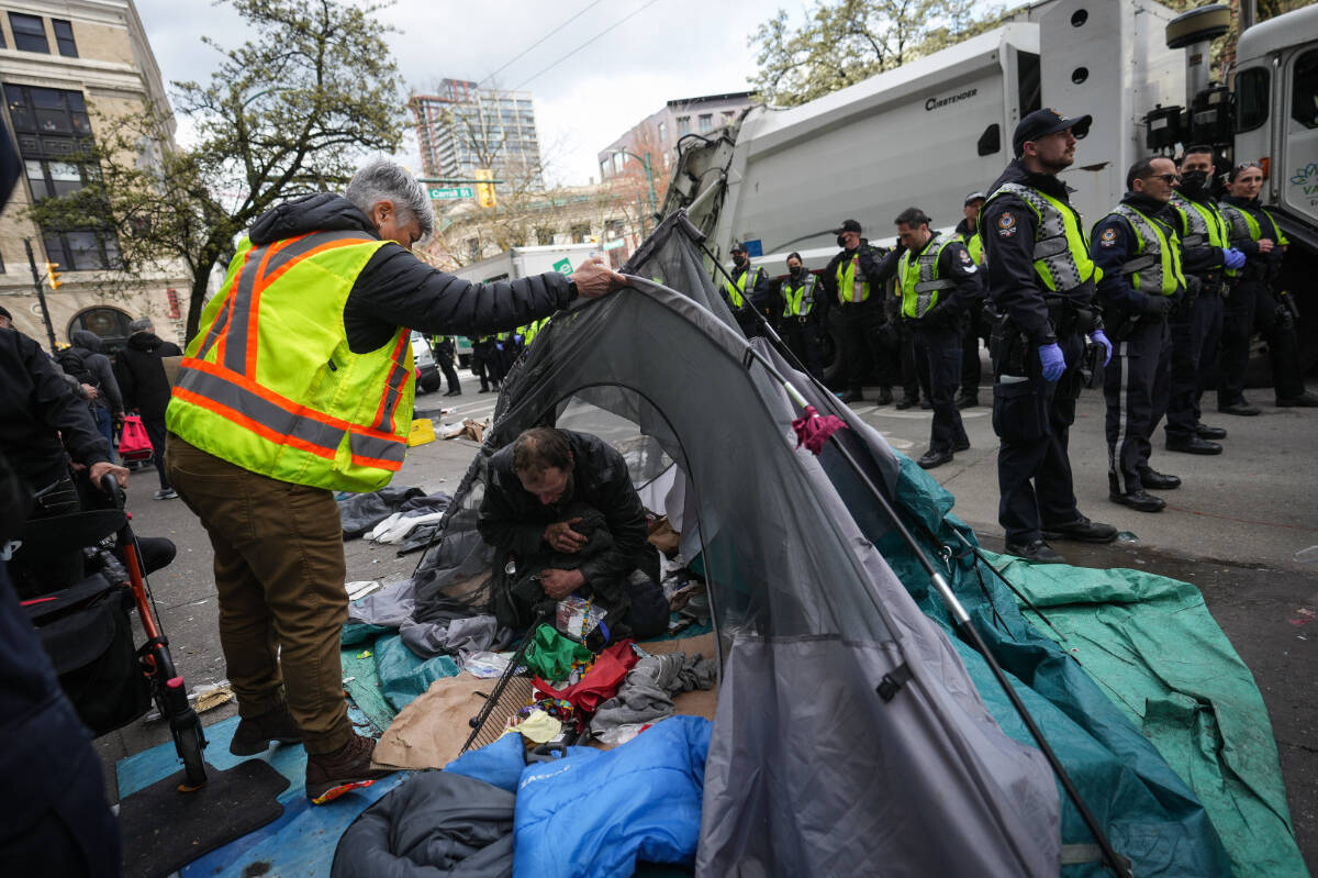 A man is seen inside his tent as vancouver police officers stand by while city workers clear an encampment on East Hastings Street in the Downtown Eastside of Vancouver, B.C., Wednesday, April 5, 2023. Vancouver police officers have been deployed to a tent encampment on the city’s Downtown Eastside with the aim of shutting down the site to campers. THE CANADIAN PRESS/Darryl Dyck
