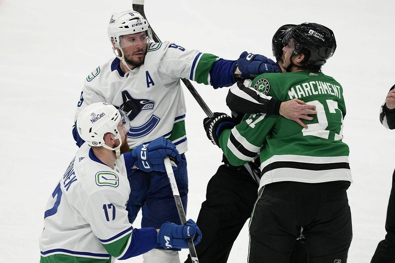An official holds Dallas Stars’ Mason Marchment (27) back as he argues with Vancouver Canucks’ Filip Hronek (17) and J.T. Miller (9) in the second period of an NHL hockey game in Dallas, Thursday, Dec. 21, 2023. (AP Photo/Tony Gutierrez)