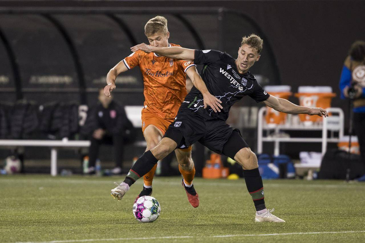 Forge FC midfielder Noah Jensen (left) fights for a ball with Cavalry FC defender Daan Klomp (4) during Canadian Premier League finals soccer action in Hamilton on Saturday, Oct. 28, 2023. THE CANADIAN PRESS/Nick Iwanyshyn