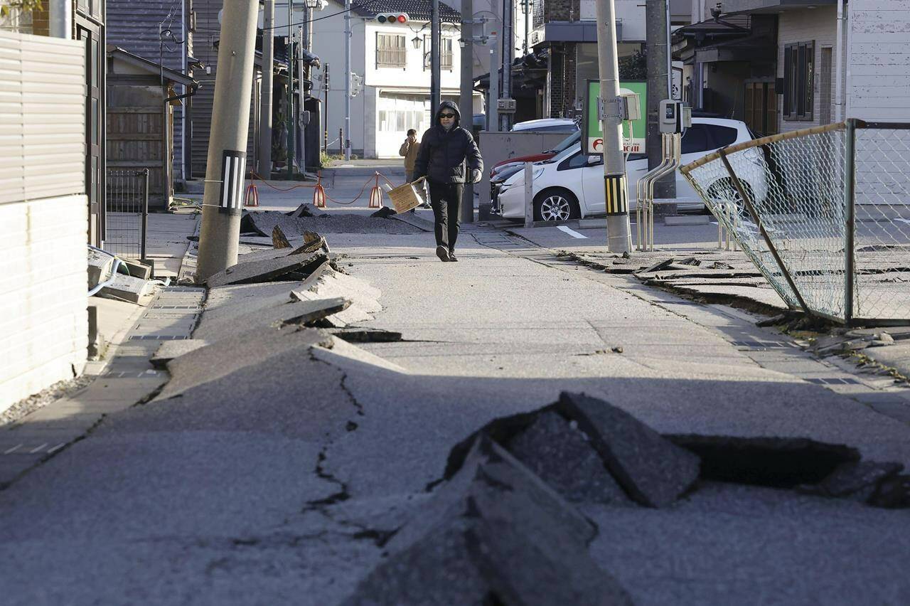 A person walks on a street damaged by an earthquake in Hakui, Ishikawa prefecture, Japan Tuesday, Jan. 2, 2024. A series of powerful earthquakes in western Japan damaged homes, cars and boats, with officials warning people on Tuesday to stay away from their homes in some areas because of a continuing risk of major quakes and tsunamis. (Kyodo News via AP)
