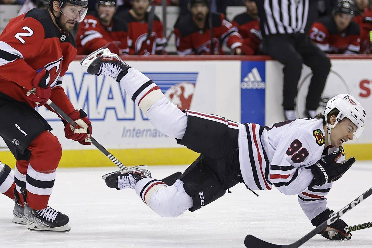 Chicago Blackhawks center Connor Bedard falls to the ice after being checked by New Jersey Devils defenseman Brendan Smith (2) during the first period of an NHL hockey game Friday, Jan. 5, 2024, in Newark, N.J. (AP Photo/Adam Hunger)
